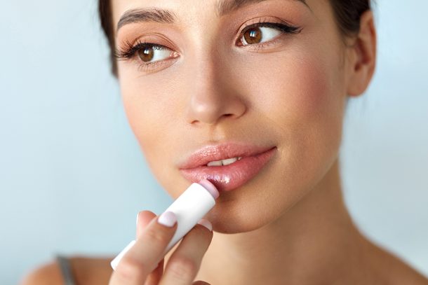 Donna mora che esamina il modo in cui ottenere delle belle labbra carnose applicando il balsamo labbra di fronte allo specchio