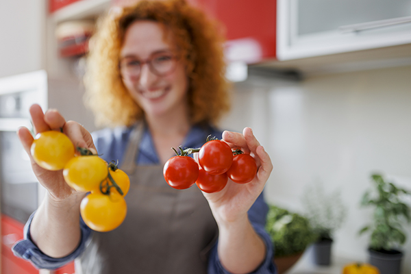 Donna in cucina che tiene in mano due grappoli di pomodori, un cibo che può essere mangiato con la pancreatite