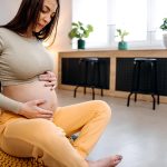 Donna incinta, con le mani sulla pancia, che si prende cura del dolore alle gengive attraverso pratiche di relax in casa