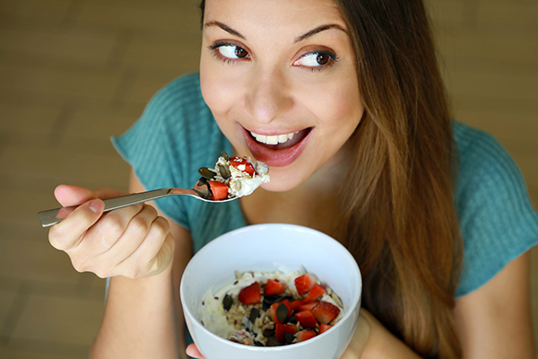 Donna che a colazione si nutre di semi di chia e dei suoi infiniti benefici, aggiunti nella ciotola insieme a yogurt, fragole e altri cereali