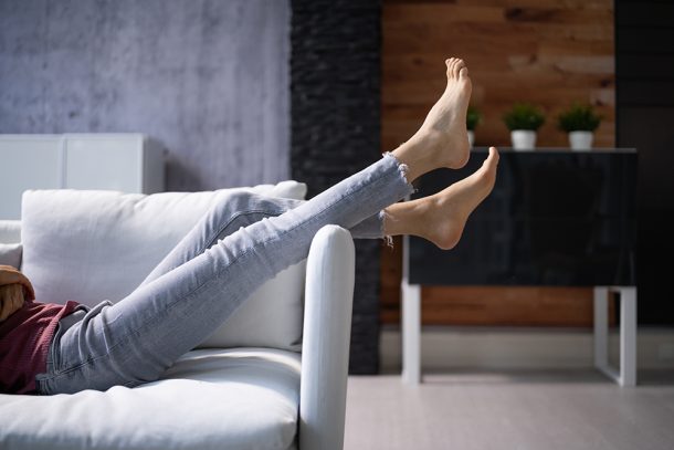Donna sdraiata supina sul divano con le gambe alzate per fornire sollievo ai piedi gonfi