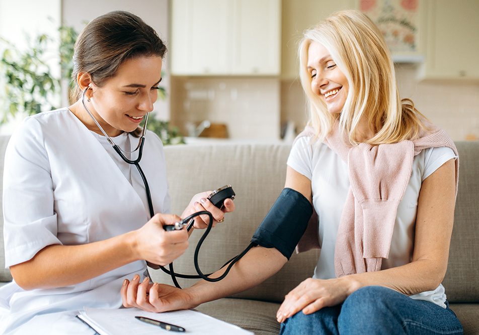 donna-senior-facendo-gesto-del-cuore-pendendosi-cura-delle-arterie-coronarie (3) Paziente con sintomi di coronarie ostruite che misura la pressione nel salotto di casa con l’ausilio dell’infermiera