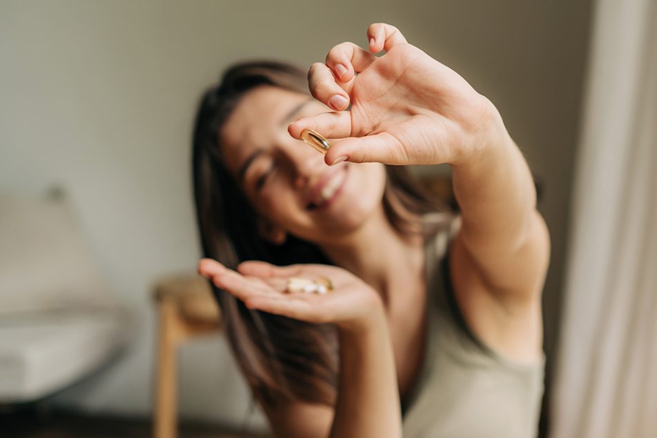 Donna sorridente nel confortevole salotto di casa che tiene in mano un integratore con Omega 3