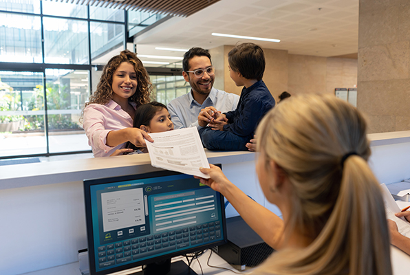 Giovane famiglia che prenota alla reception dello studio medico i prossimi appuntamenti per i figli con esenzione 013