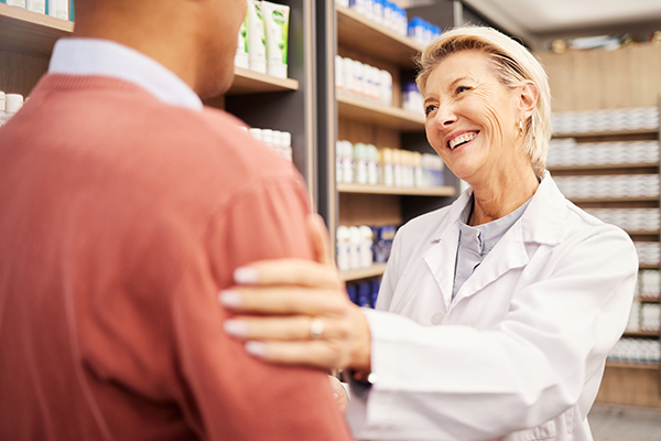 Farmacista che fornisce al cliente informazioni sul principio attivo dell’Oki, porgendogli una mano sulla spalla in segno di fiducia