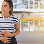 Giovane donna si tocca l'addome per sintomi pancreatite