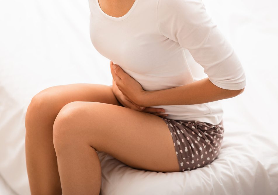 Giovane donna seduta sul letto si tiene la pancia cercando di capire le cause del suo gonfiore addominale