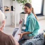 Infermiera sorridente che assiste un uomo anziano in salotto per indossare delle calze a compressione