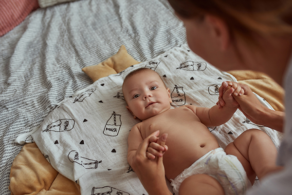 Madre che cambia il pannolino al suo neonato vispo e curioso, che soffre temporaneamente di diarrea, mentre è sdraiato sul materassino per fasciatoio