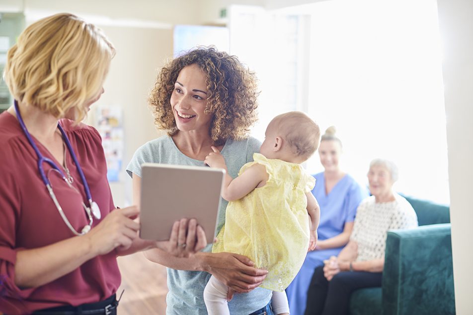 Giovane madre che consulta il personale della reception dello studio medico, in possesso dei requisiti per l’esenzione E03 per la figlia
