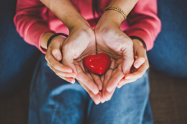 Madre e figlio con le mani giunte che tengono un cuore rosso promuovendo la donazione degli organi