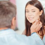 Medico che conversa con una giovane paziente durante la visita medica, toccandole i linfonodi del collo per verificare lo stato di salute