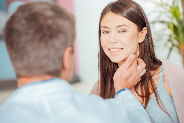 Medico che conversa con una giovane paziente durante la visita medica, toccandole i linfonodi del collo per verificare lo stato di salute