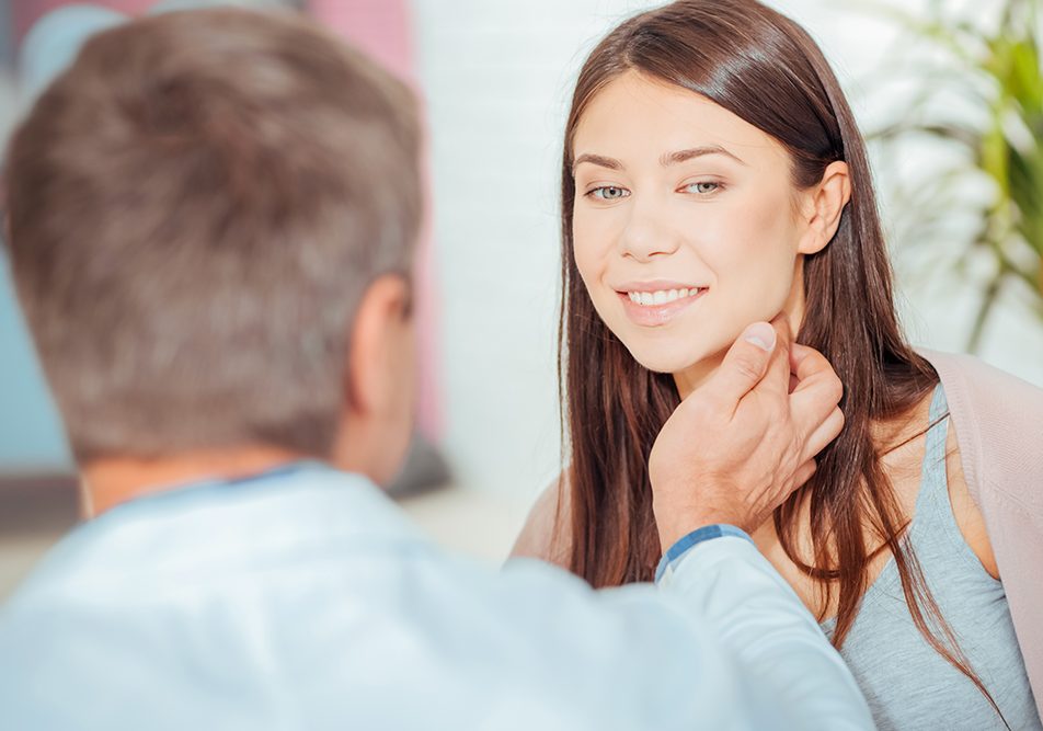 Medico che conversa con una giovane paziente durante la visita medica, toccandole i linfonodi del collo per verificare lo stato di salute