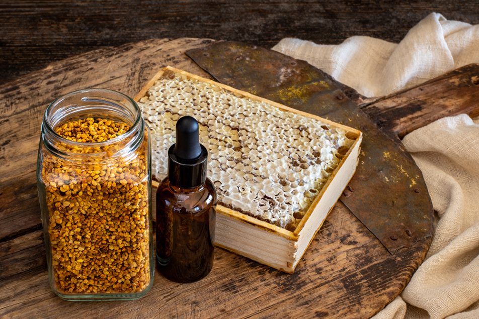 Miele biologico e boccetta contenete polline e propoli, antibiotico naturale, su pala di legno