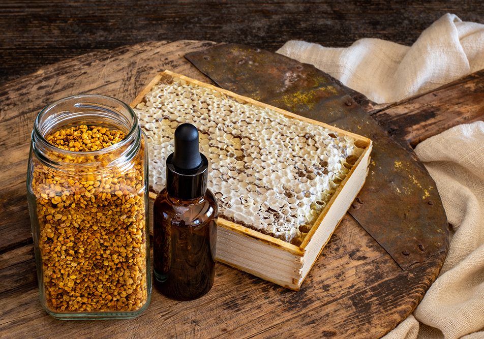 Miele biologico e boccetta contenete polline e propoli, antibiotico naturale, su pala di legno