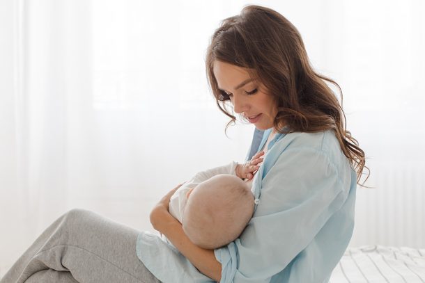 neomamma-con-ipoprolattinemia-allattando-bebe Neomamma che soffre di ipoprolattinemia allatta il suo bebè mentre è seduta ai bordi del letto indossando comodi indumenti di cotone