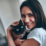 Padrona che tiene in braccio il suo gatto siamese che accusa sintomi di pancreatite, accanto alla finestra del salotto