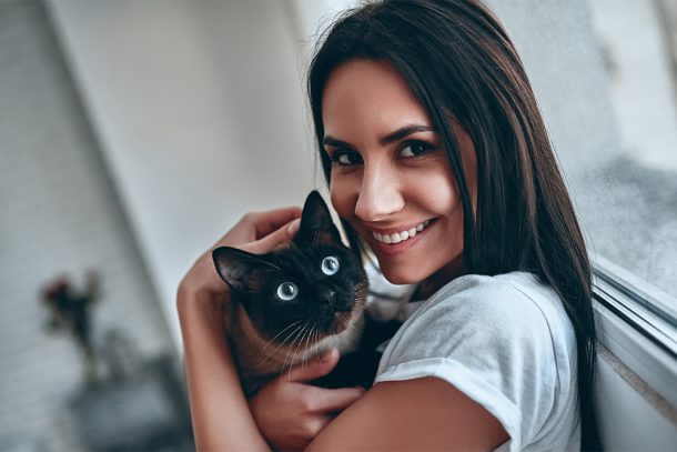 padrona-tenendo-in-braccio-gatto-siamese-con-sintomi-pancreatite-a-casa Padrona che tiene in braccio il suo gatto siamese che accusa sintomi di pancreatite, accanto alla finestra del salotto