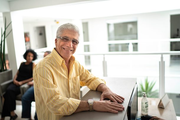 Paziente senior alla reception della clinica medica che sporge alla segretaria l’esenzione per patologia di cui beneficia