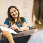 Paziente alla reception della clinica medica che compila la documentazione sanitaria in seguito alla scadenza dell’esenzione C02, aiutata da una segretaria