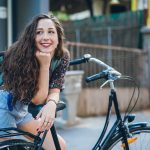 Ragazza in sosta lungo una via cittadina che si appoggia al sellino della sua bicicletta riflettendo se salire o meno per via dei dolori da ciclo senza ciclo