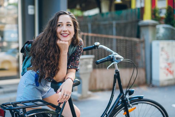 Ragazza in sosta lungo una via cittadina che si appoggia al sellino della sua bicicletta riflettendo se salire o meno per via dei dolori da ciclo senza ciclo