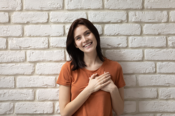 Ragazza sorridente con problemi alle arterie coronarie che mette le mani sul petto, nella zona del cuore