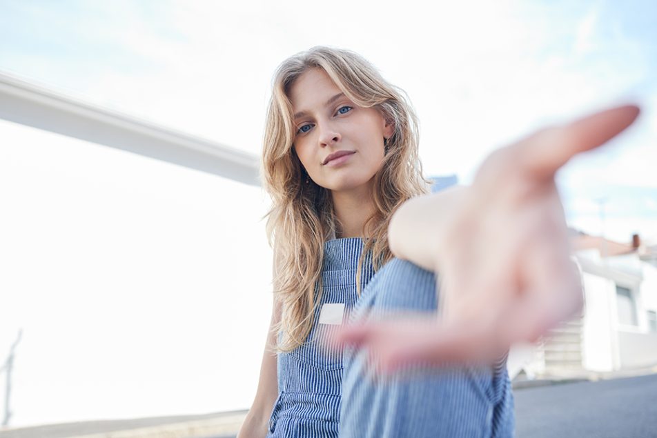 Ragazza su una terrazza cittadina, dopo essere stata sottoposta ad un trapianto, che lancia un messaggio di incoraggiamento con una mano protesa in avanti