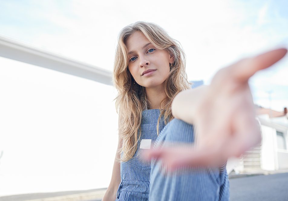 Ragazza su una terrazza cittadina, dopo essere stata sottoposta ad un trapianto, che lancia un messaggio di incoraggiamento con una mano protesa in avanti