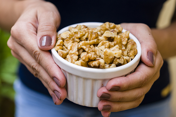 Donna che tiene in mano una ciotola con noci sgusciate, un alimento ricco di Omega 3 di cui ella può trarre i benefici per la sua salute