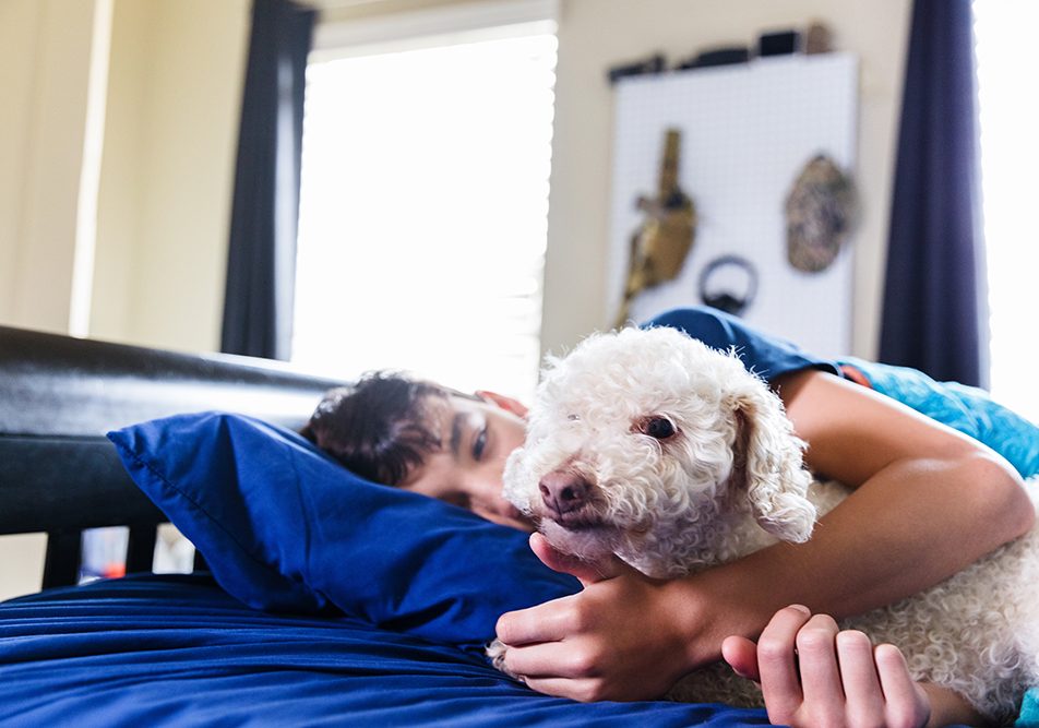 Ragazzo che coccola il suo cane con il raffreddore nel suo letto, mentre riposano insieme