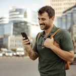 Uomo, con sistema endocrino in salute, cammina in citta mentre guarda il suo smartphone