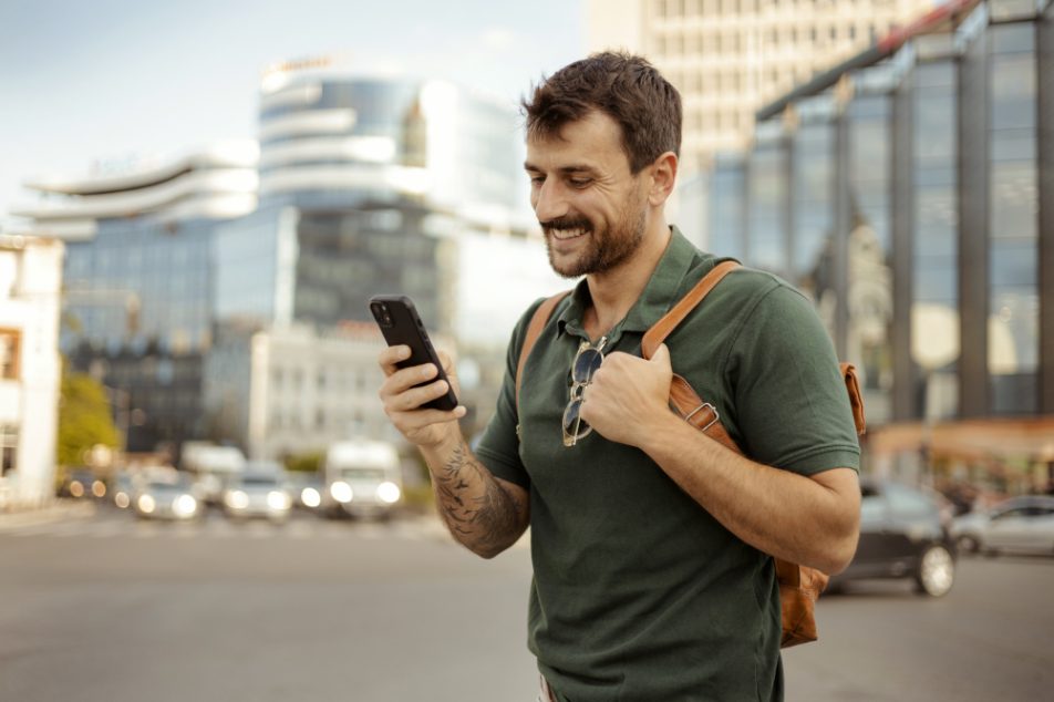 Uomo, con sistema endocrino in salute, cammina in citta mentre guarda il suo smartphone