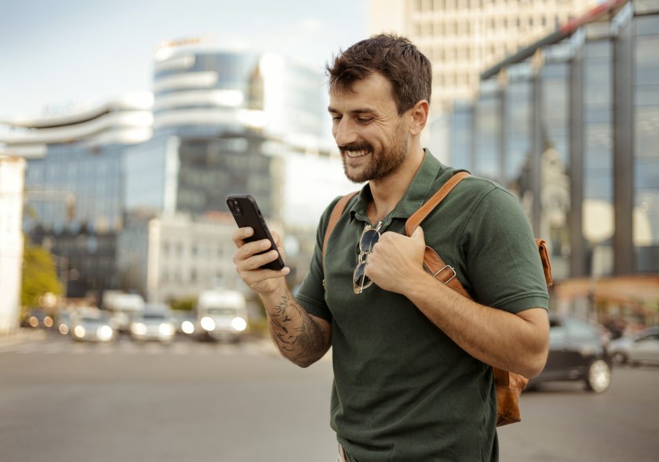 Uomo, con sistema endocrino in salute, cammina in citta mentre guarda il suo smartphone