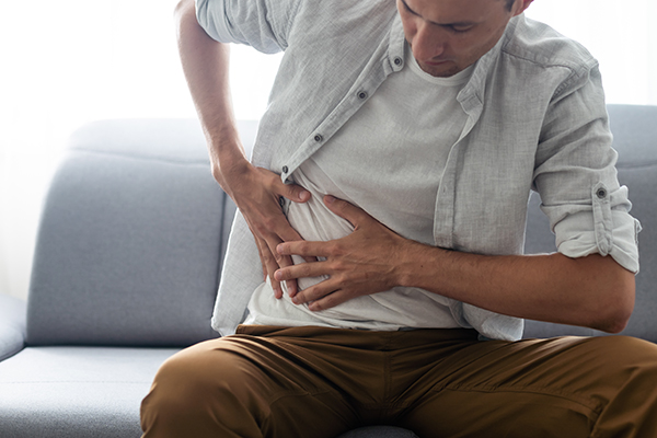 Uomo seduto sul divano di casa che avverte dolore al pancreas e allo stomaco dopo avere attenzionato feci scure e verdi