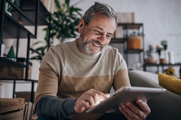 Uomo maturo a casa che si informa online, attraverso il suo tablet, dell’esenzione ticket di cui potrebbe beneficiare