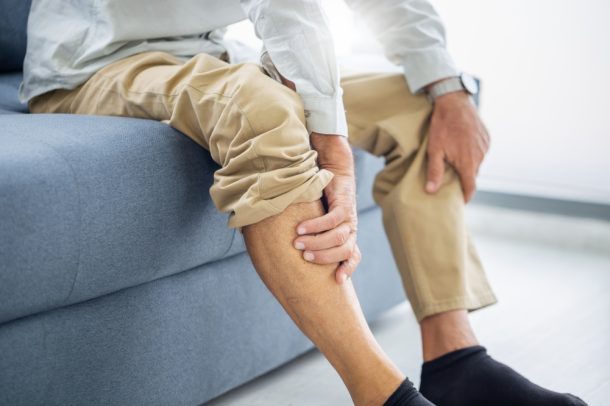 Uomo maturo seduto sul divano si massaggia le caviglie gonfie