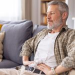 Uomo maturo seduto sul divano con tumore al pancreas mentre si tocca l'addome