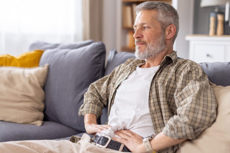 Uomo maturo seduto sul divano con tumore al pancreas mentre si tocca l'addome