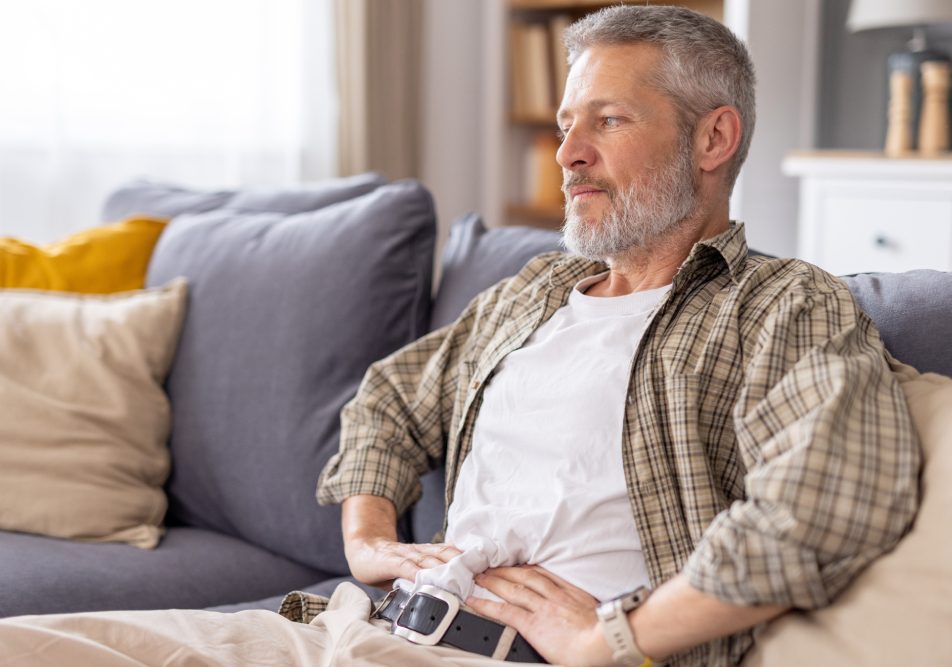 Uomo maturo seduto sul divano con tumore al pancreas mentre si tocca l'addome