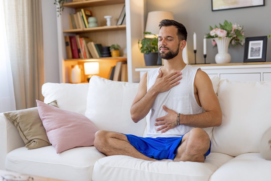 Uomo che medita sul divano con le mani sul petto e sull’addome, prendendosi cura del tumore al pancreas