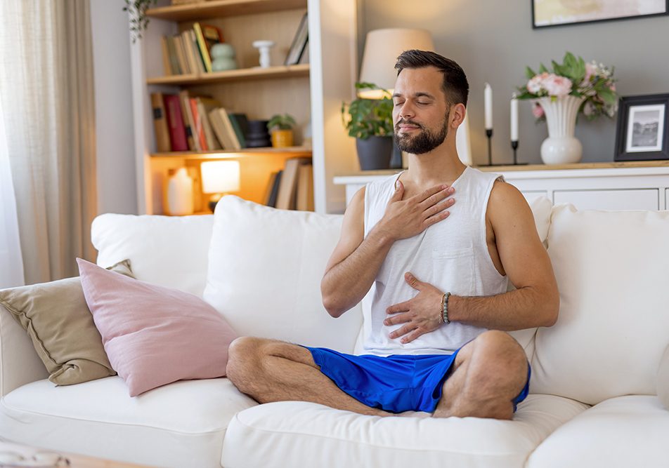 Uomo che medita sul divano con le mani sul petto e sull’addome, prendendosi cura del tumore al pancreas