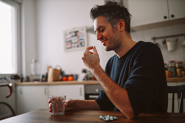 Uomo seduto al tavolo della cucina che assume farmaci per la cura del dolore alla cervicale