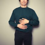 Uomo che si tocca lo stomaco e la cistifellea con le mani, avvertendo dolore causato dai calcoli alla colecisti