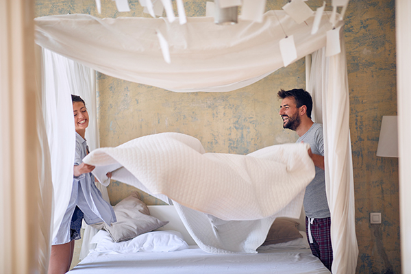 Coppia di innamorati mentre rifà il letto, che si prende cura dell’ambiente adibito al riposo al fine di favorire le modalità per riuscire a dormire velocemente