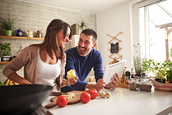 Coppia insieme in cucina che prepara una ricetta sana ed equilibrata con peperoni, funghi e altri ingredienti vegetali, mettendo in pratica i consigli su come abbassare i trigliceridi alti
