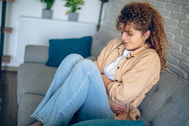 donna-a-casa-avvertendo-cistite-interstiziale-sintomi Donna rannicchiata sul divano di casa che avverte i sintomi della cistite interstiziale