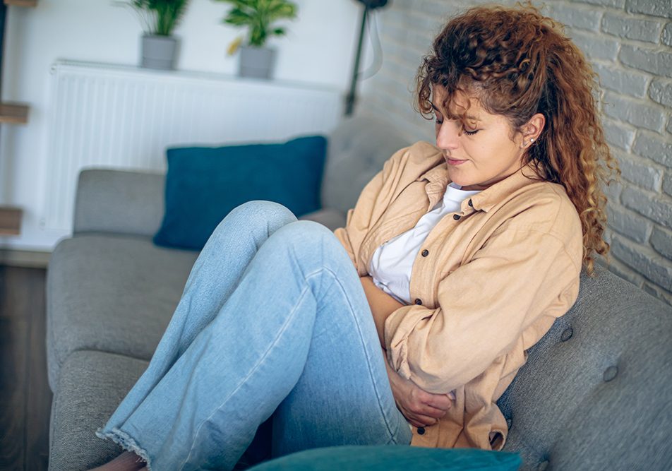 donna-a-casa-avvertendo-cistite-interstiziale-sintomi Donna rannicchiata sul divano di casa che avverte i sintomi della cistite interstiziale