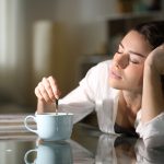 Al mattino, una donna mescola il caffè in cucina, mentre riflette sulle conseguenze psicologiche del dormire poco